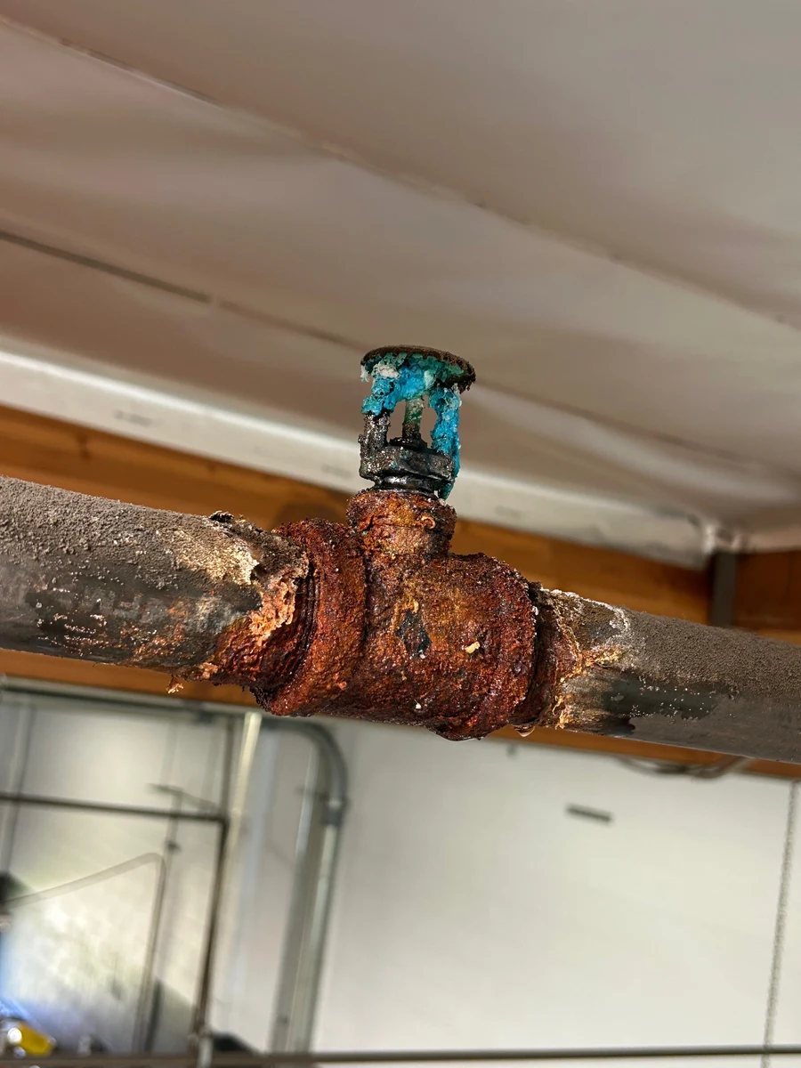 Corroded fire sprinkler pipe tee showing copper oxidation and rust buildup