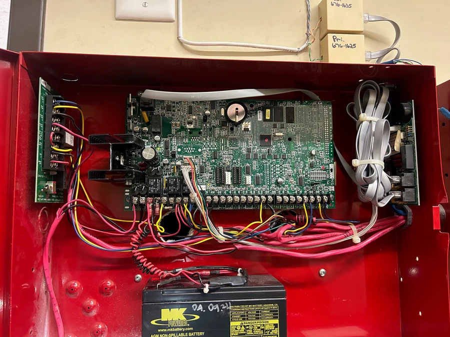 Opened fire alarm control panel showing the main circuit board, wiring terminals, and backup battery