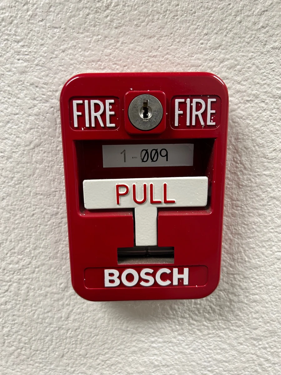 Red Bosch manual fire alarm pull station mounted on a white wall, its white PULL lever and keyed reset visible