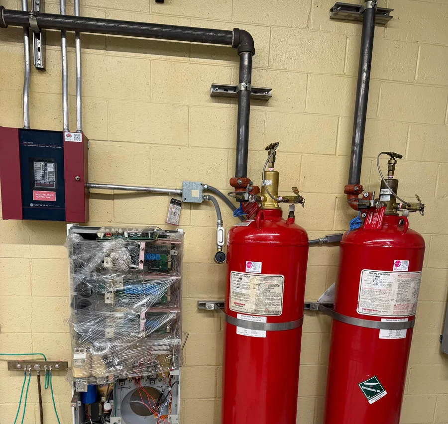 Two FM-200 clean agent suppression cylinders installed against a block wall beside a fire alarm control panel